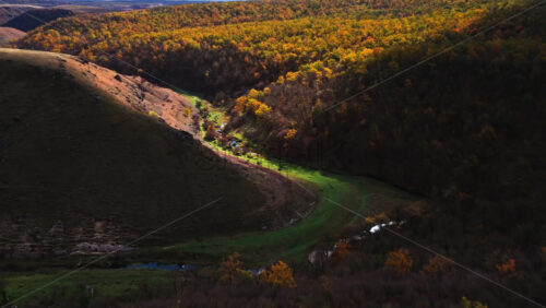 Video - Aerial drone view of a curving valley with a small river flowing through green and yellow trees in rural Moldova