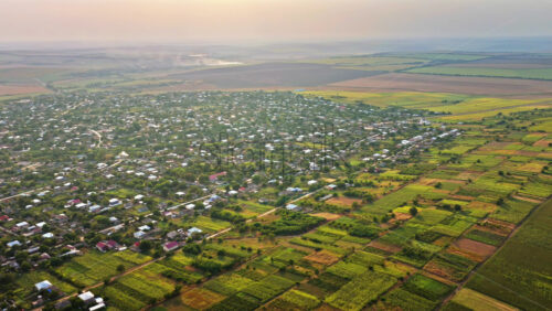 Video - Aerial drone view showing a Moldovan village surrounded by vast farmlands and open fields under a hazy autumn sky