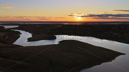 Video - Aerial drone view of a winding river reflecting the warm sunset light over Moldova's rolling hills and distant villages