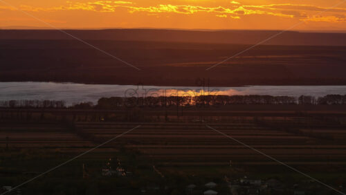 Video - Aerial drone view of a winding river reflecting the warm sunset light over Moldova's rolling hills and distant villages