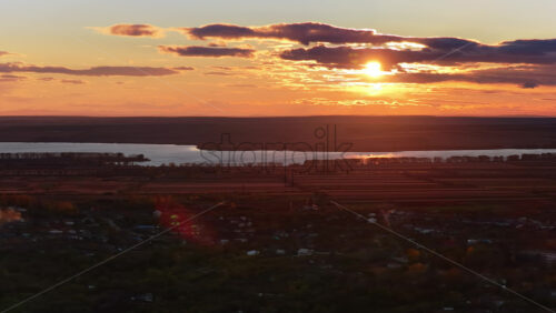 Video - Aerial drone view of a winding river reflecting the warm sunset light over Moldova's rolling hills and distant villages