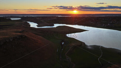 Video - Aerial drone view of a winding river reflecting the warm sunset light over Moldova's rolling hills and distant villages