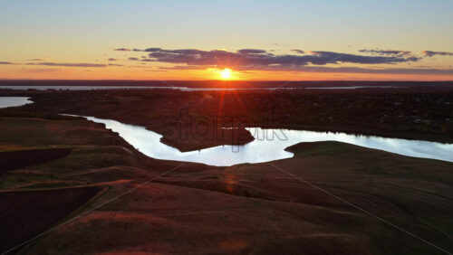 Video - Aerial drone view of a winding river reflecting the warm sunset light over Moldova's rolling hills and distant villages