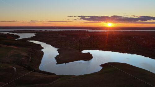 Video - Aerial drone view of a winding river reflecting the warm sunset light over Moldova's rolling hills and distant villages