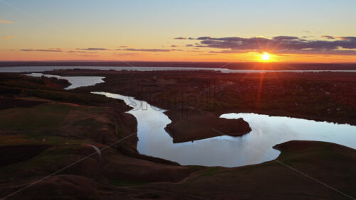 Video - Aerial drone view of a winding river reflecting the warm sunset light over Moldova's rolling hills and distant villages
