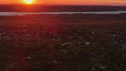 Video - Aerial drone view of a Moldovan village at sunset with the river and fields glowing in warm orange tones