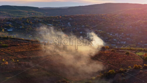 Video - Aerial drone view of smoke rising from farmlands in Moldova at golden hour