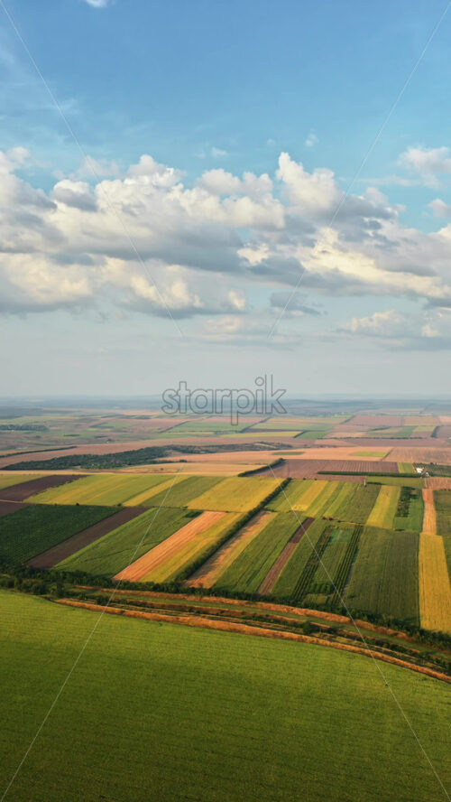 Video - Aerial drone view of the vast Moldovan countryside with colorful patchwork fields stretching to the horizon under a partly cloudy sky. Vertical