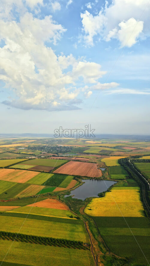 Video - Aerial drone view of the vast Moldovan countryside with colorful patchwork fields stretching to the horizon under a partly cloudy summer sky