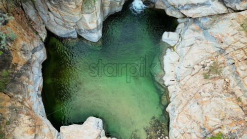 Video - Aerial drone view of a small waterfall cascading between rocks surrounded by desert vegetation and palm trees in Baja California Sur, Mexico