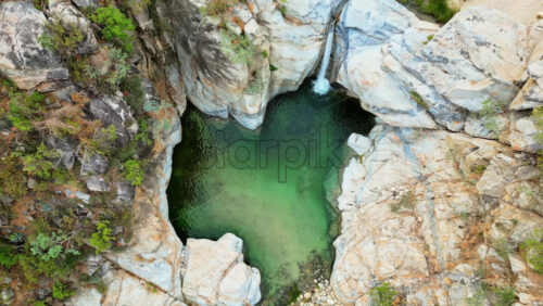 Video - Aerial drone view of a canyon with a small waterfall falling into a natural pool surrounded by rocky cliffs in Baja California, Mexico