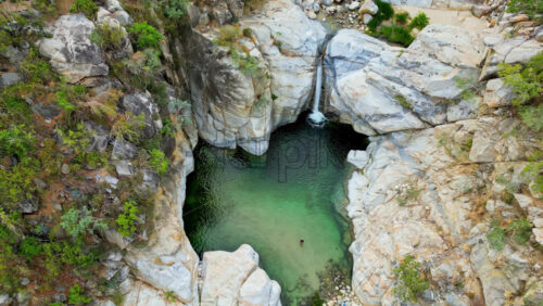 Video - Aerial drone view of a canyon with a small waterfall falling into a natural pool surrounded by rocky cliffs in Baja California, Mexico
