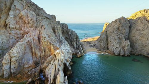 Video - Aerial drone view revealing a secluded sandy cove nestled between towering cliffs near El Arco in Cabo San Lucas