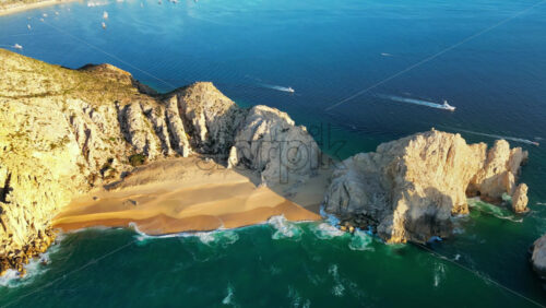 Video - Aerial drone view of Lover's Beach, one of the most famous beaches in Cabo San Lucas, framed by monumental rock cliffs and emerald waters