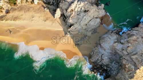 Video - Aerial drone view of Lover's Beach, one of the most famous beaches in Cabo San Lucas, framed by monumental rock cliffs and emerald waters