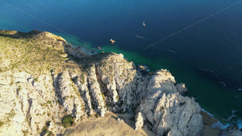 Video - Aerial drone view of Lover's Beach, one of the most famous beaches in Cabo San Lucas, framed by monumental rock cliffs and emerald waters