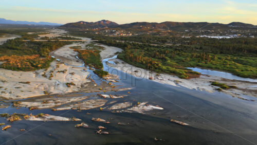 Video - Aerial drone view of a calm river meeting the sea, surrounded by lush green vegetation and distant hills