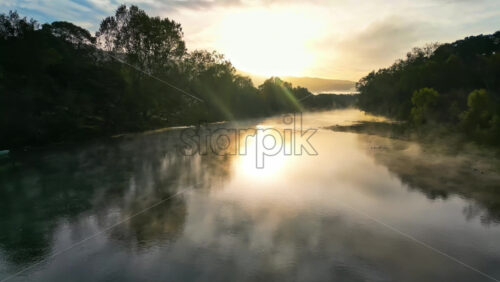 Video - Aerial drone view of a river at sunrise with morning mist floating above the water and golden sunlight reflecting on the surface in Baja