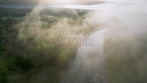 Video - Aerial drone view of a river at sunrise with morning mist floating above the water and golden sunlight reflecting on the surface in Baja
