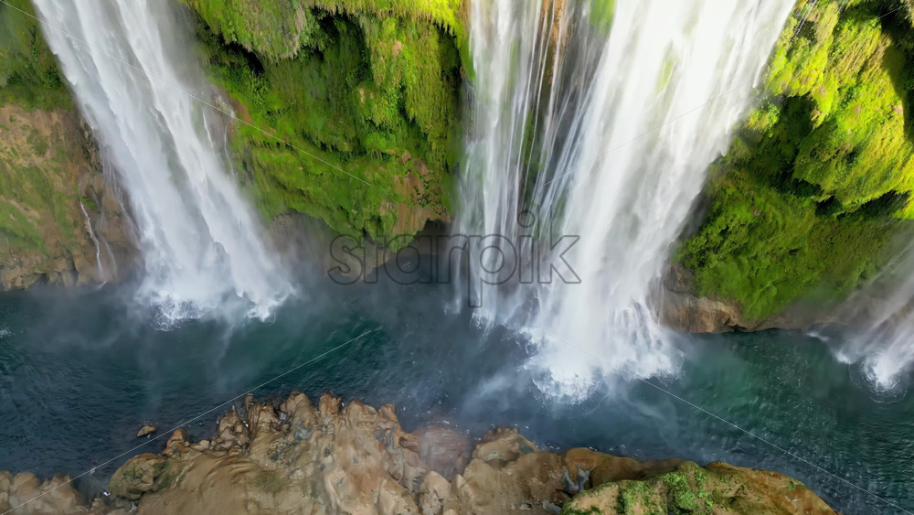 Video - Aerial drone view of Tamul Waterfall cascading down green cliffs into a turquoise pool below
