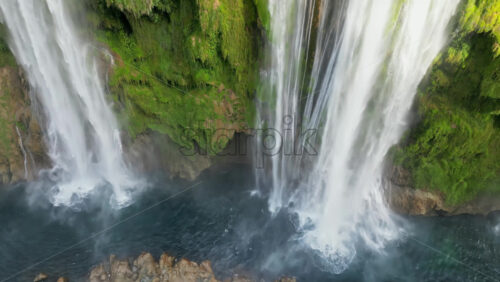 Video - Aerial drone view of Tamul Waterfall cascading down green cliffs into a turquoise pool below