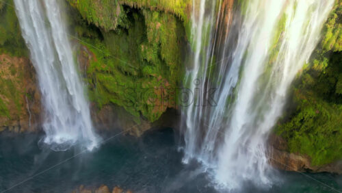 Video - Aerial drone view of Tamul Waterfall cascading down green cliffs into a turquoise pool below