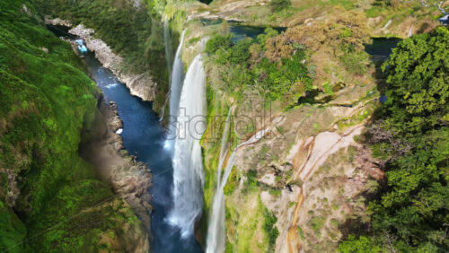 Video - Aerial drone view of Tamul Waterfall cascading down green cliffs into a turquoise pool below