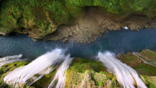 Video - Aerial drone view of several powerful waterfalls dropping into a narrow canyon with green moss and rocks