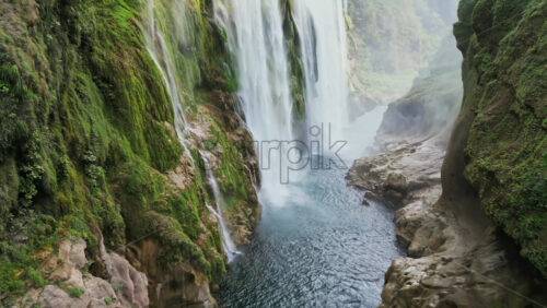 Video - Aerial drone view of Tamul Waterfall cascading down green cliffs into a turquoise pool below