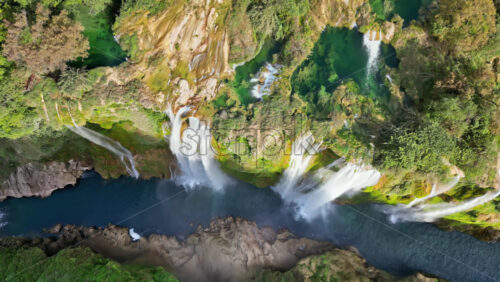 Video - Aerial drone view of Tamul Waterfall cascading down green cliffs into a turquoise pool below