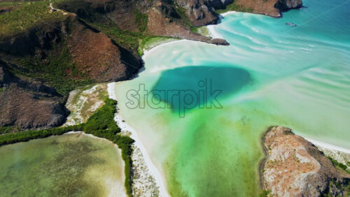 Video - Aerial drone view of a coastal lagoon with turquoise and green tones surrounded by dry rocky hills and vegetation in Baja California Sur