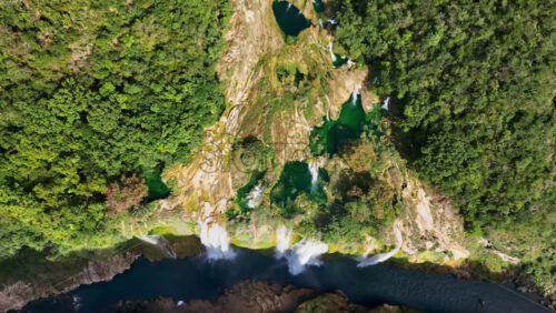 Video - Aerial drone view of Tamul Waterfall cascading down green cliffs into a turquoise pool below