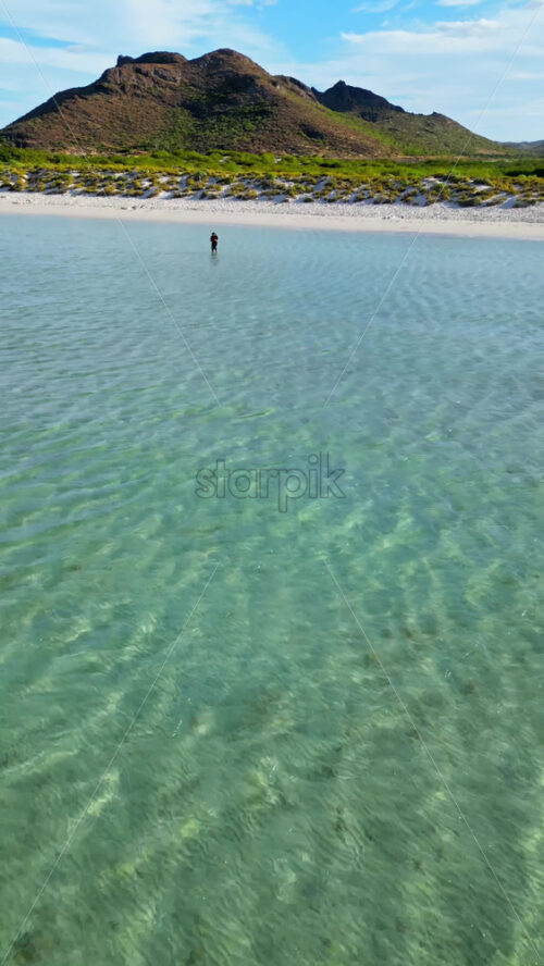Video - Aerial drone view of a person standing in shallow turquoise water at Balandra Beach , near La Paz, Mexico. Vertical
