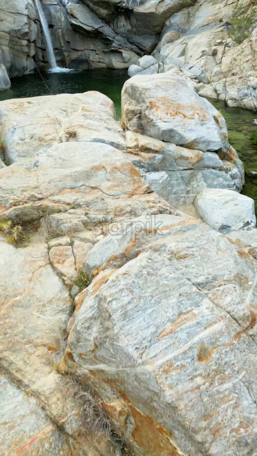 Video - Aerial drone view of a calm natural pool surrounded by large gray rocks and crystal clear water. Vertical