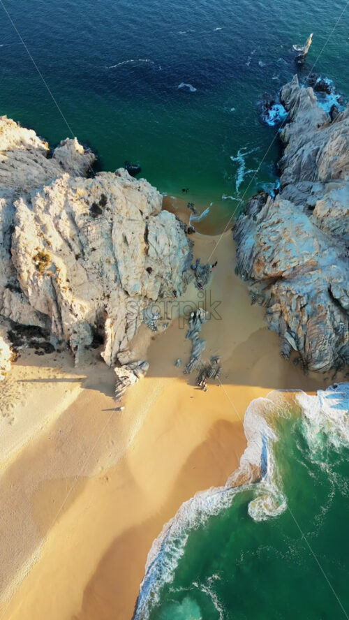 Video - Aerial drone view of Lover's Beach, one of the most famous beaches in Cabo San Lucas, framed by monumental rock cliffs and emerald waters. Vertical