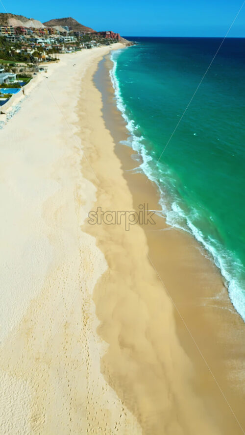Video - Aerial drone view above Costa Azul beach, showing the vast turquoise ocean meeting golden sand and coastal cliffs. Vertical