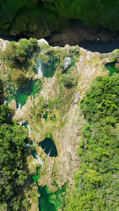 Video - Aerial drone view of a stunning canyon with turquoise waterfalls and layered rock formations surrounded by green forest in Mexico. Vertical