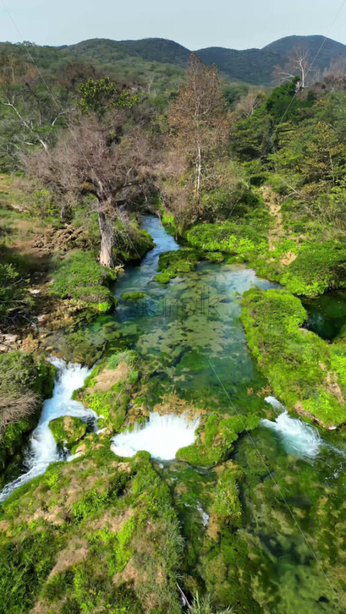Video - Aerial drone view of a stunning canyon with turquoise waterfalls and layered rock formations surrounded by green forest in Mexico. Vertical