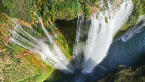 Video - Aerial drone view of Tamul Waterfall cascading down green cliffs into a turquoise pool below in slow motion