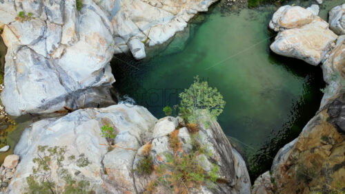 Video - Aerial drone view of a small waterfall cascading over smooth rocks, surrounded by palm trees and wild plants in slow motion