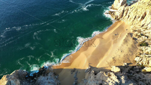Video - Aerial drone view of Lover's Beach, one of the most famous beaches in Cabo San Lucas, framed by monumental rock cliffs and emerald waters in slow motion