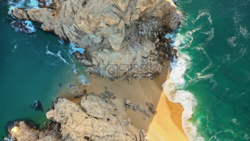 Video - Aerial drone view of Lover's Beach, one of the most famous beaches in Cabo San Lucas, framed by monumental rock cliffs and emerald waters in slow motion