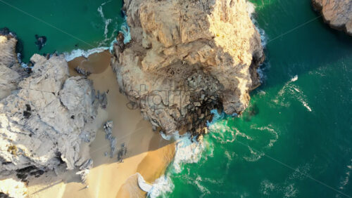 Video - Aerial drone view of Lover's Beach, one of the most famous beaches in Cabo San Lucas, framed by monumental rock cliffs and emerald waters in slow motion