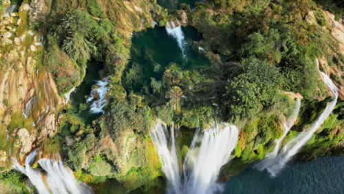 Video - Aerial drone view of Tamul Waterfall cascading down green cliffs into a turquoise pool below in slow motion