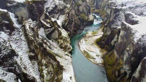 Video - Aerial drone view of Iceland's Fjaorargljufur Canyon partially covered in snow, with a winding blue river cutting through