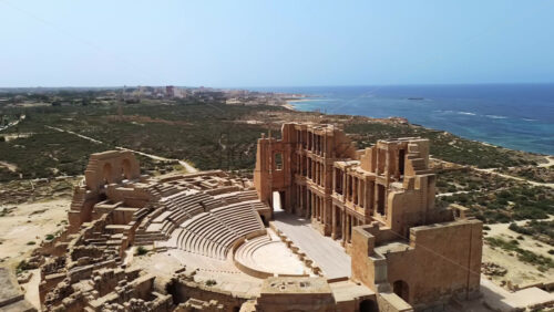 Video - Aerial drone view of the magnificent Roman Theatre of Sabratha, highlighting the detailed columns, arches, and stage area of the ancient structure