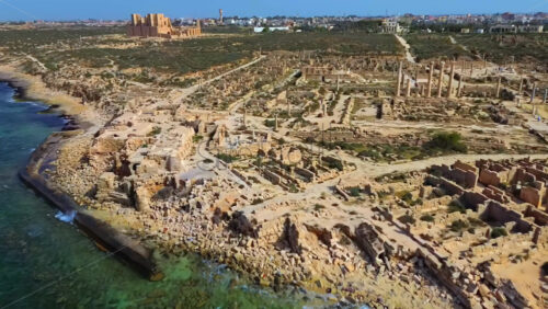 Video - Aerial drone view of Sabratha, an ancient Roman city in Libya, showing a vast archaeological site featuring temples, columns, and stone ruins that extend toward the sea