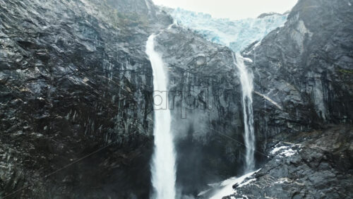 Video - Aerial drone view of twin waterfalls flowing down rocky cliffs from a massive glacier in Patagonia