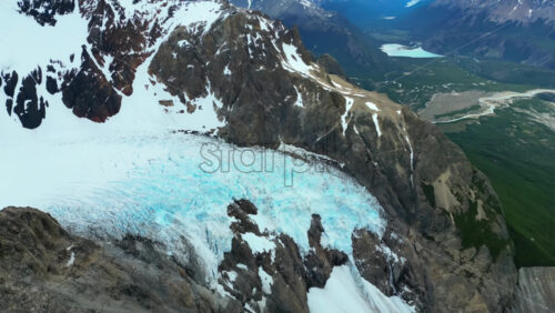 Video - Aerial drone view of a massive glacier descending between rugged mountain slopes, with sweeping views of valleys and distant lakes