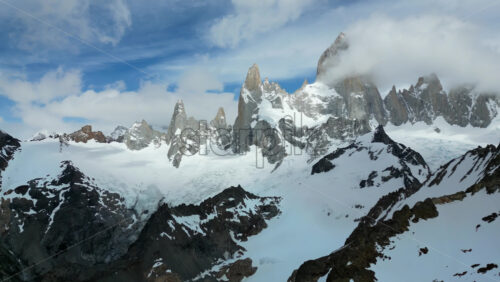 Video - Aerial drone view of a bright turquoise glacial lake nestled between steep rocky cliffs and snow covered peaks